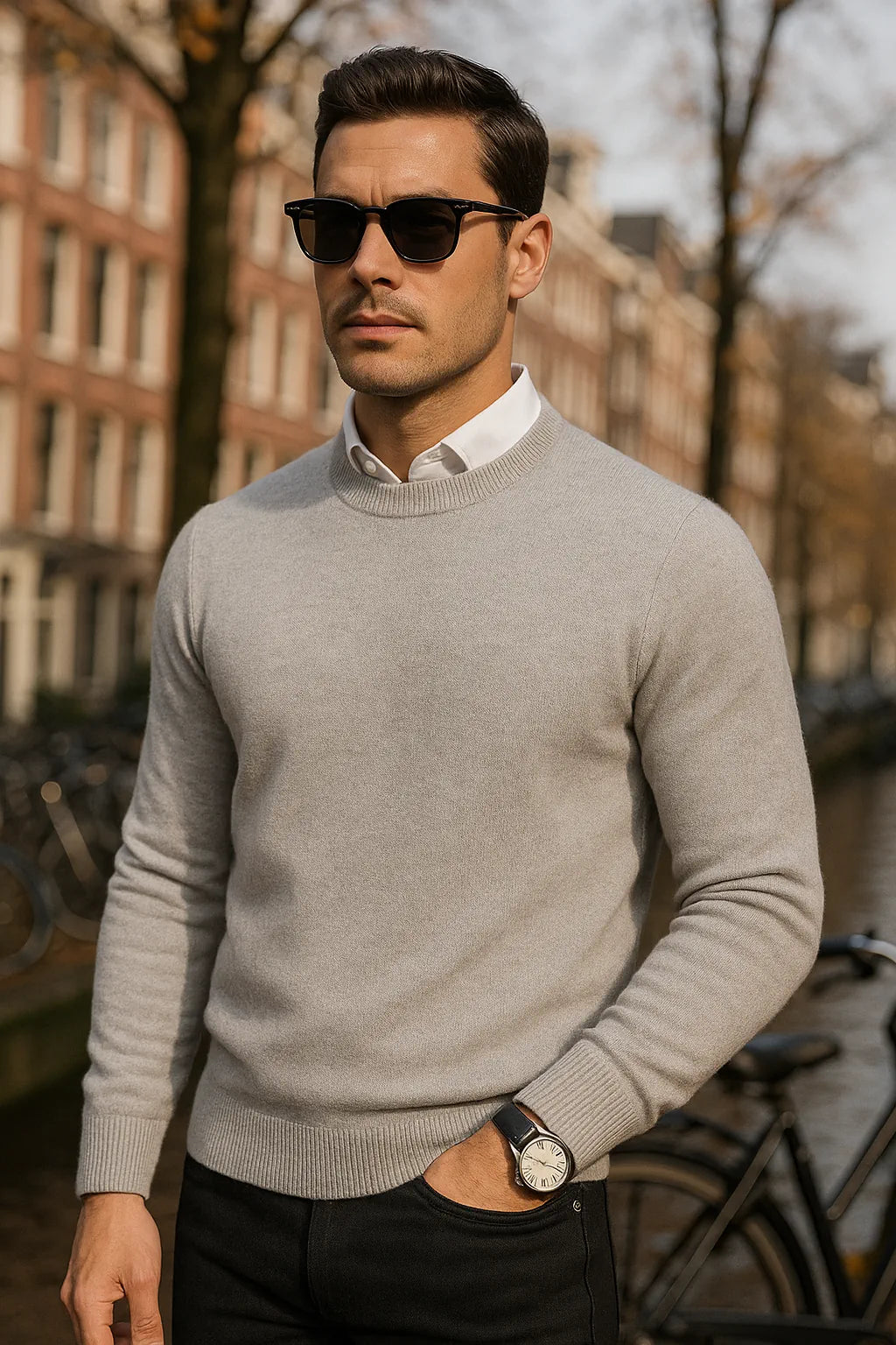 Man wearing a gray sweater and sunglasses outdoors with buildings in the background