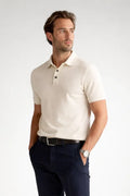 Man wearing a beige polo shirt and dark pants on a white background