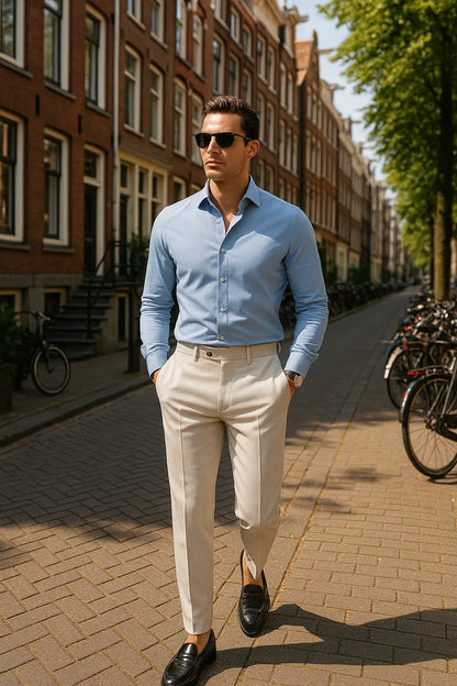 Man in a light blue shirt and beige pants walking on a street with bicycles and buildings in the background.