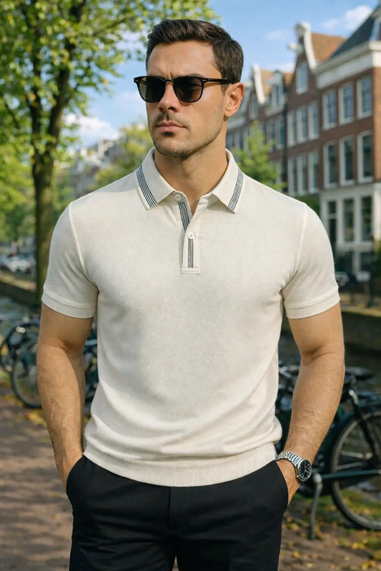 Man wearing a light-colored polo shirt and sunglasses in an urban setting with buildings and bicycles.