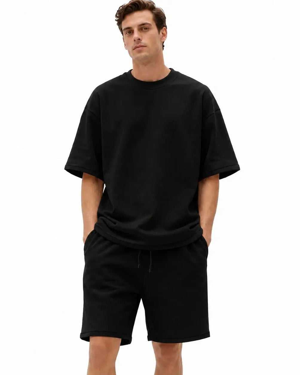 A man wearing a black oversized short-sleeve t-shirt and matching black drawstring shorts, standing against a plain white background.