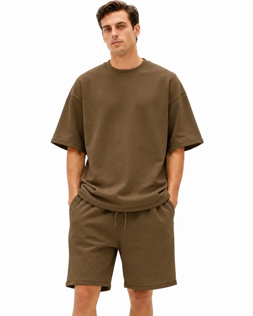 A man modeling a matching two-piece lounge set consisting of an oversized short-sleeve crewneck t-shirt and drawstring shorts in a solid olive brown color, set against a plain white background.