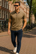 Man walking on a street wearing a brown polo shirt and navy pants.