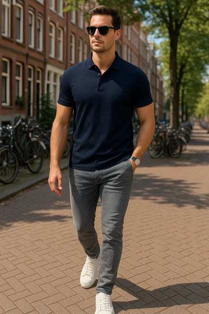 Man walking on a street wearing a navy polo shirt and gray jeans.