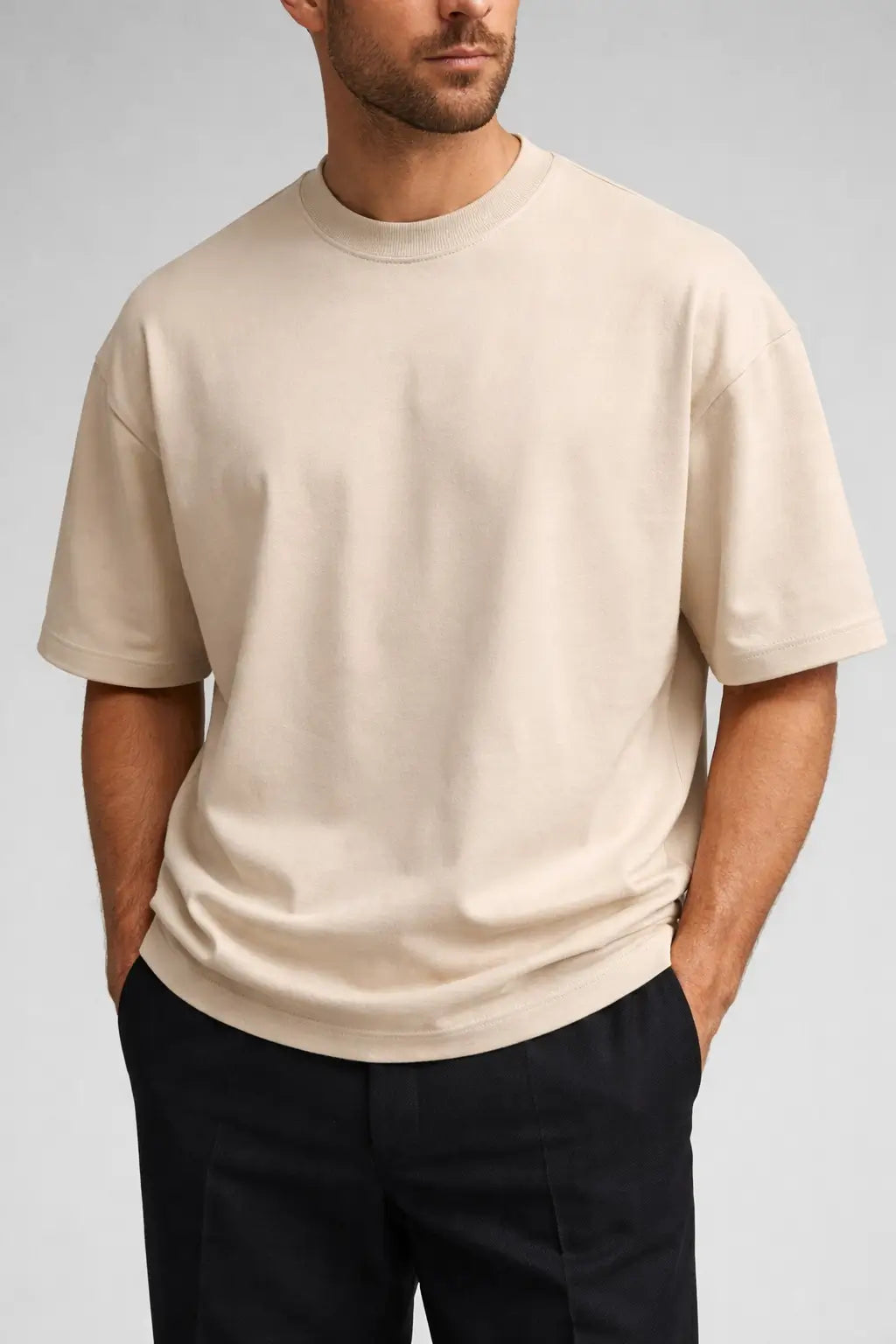Man wearing a beige t-shirt and black pants on a gray background