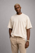 Man wearing a beige t-shirt and pants against a gray background