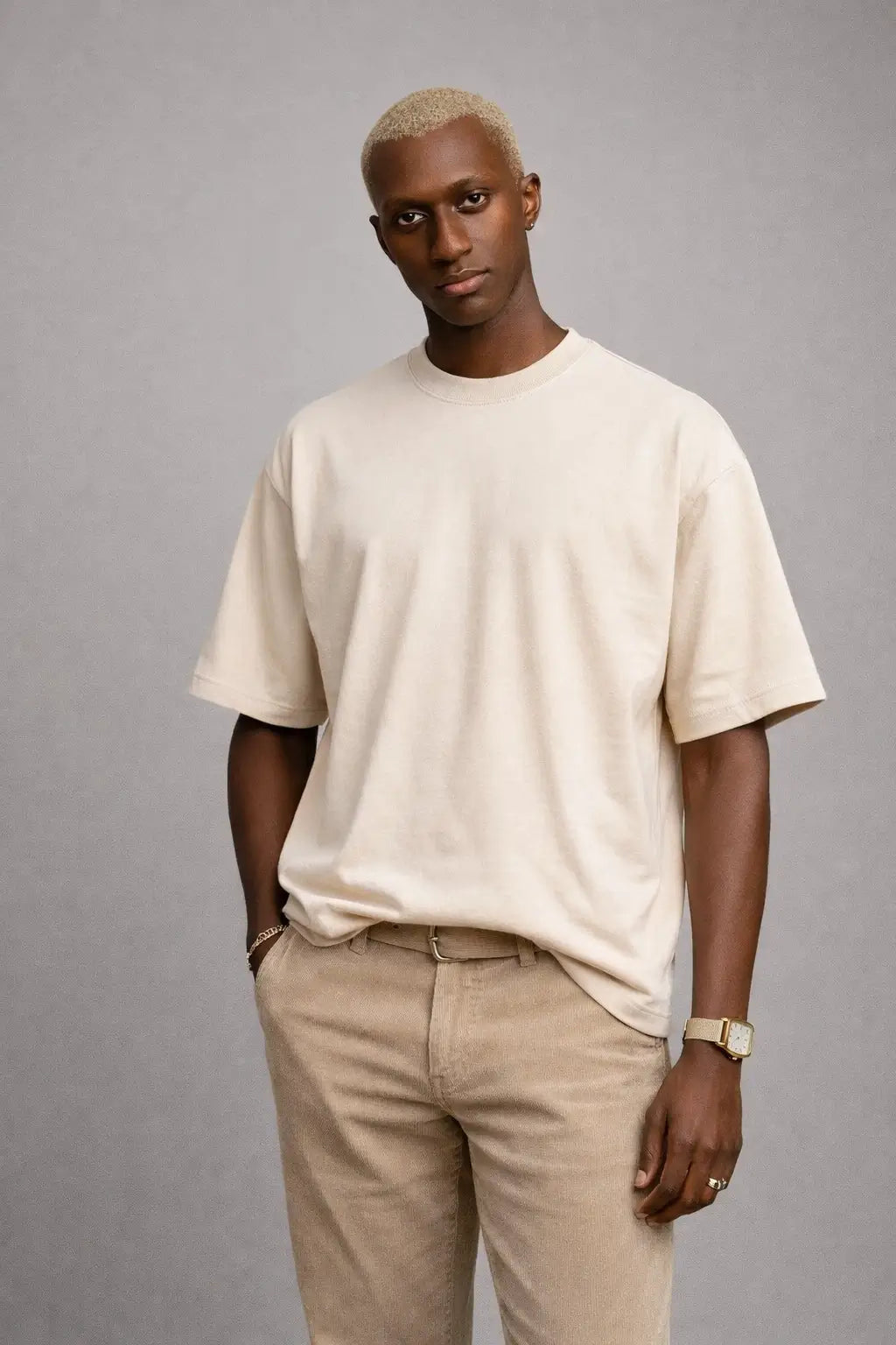 Man wearing a beige t-shirt and pants against a gray background