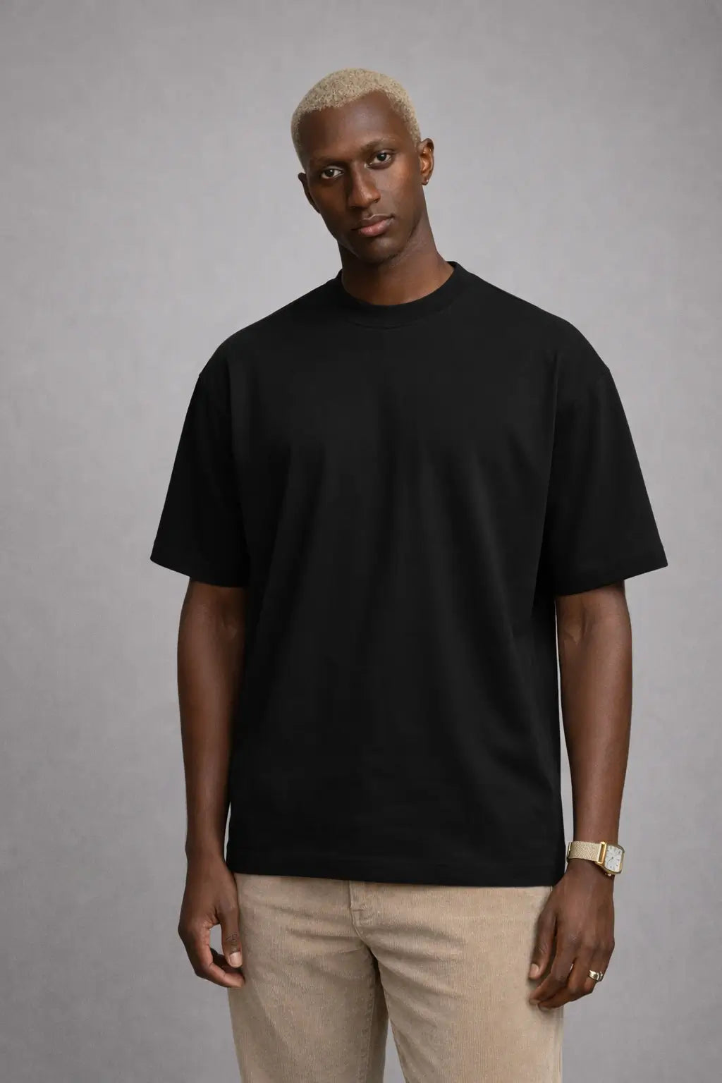 Man wearing a black t-shirt and beige pants against a gray background