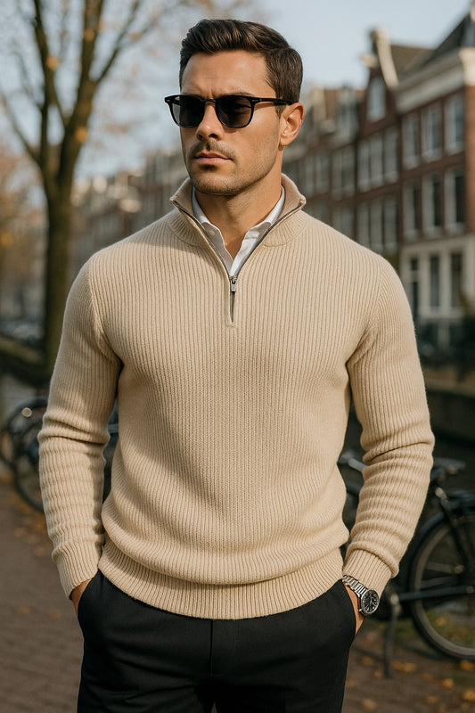 Man wearing a beige sweater and sunglasses outdoors with buildings in the background