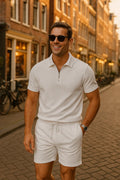 Man wearing a white polo shirt and shorts standing on a street with buildings in the background.