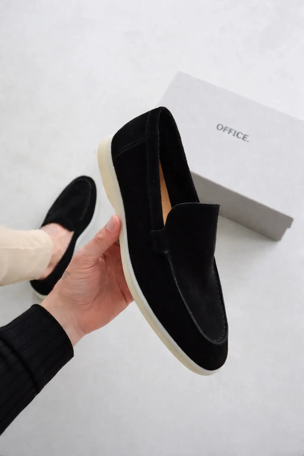 Black loafers held by a hand with a white background